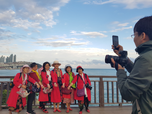중국 쓰촨에서 온 60~70대 자유여행객 6명이 지난 17일 해운대구 동백섬에서 기념 촬영을 하고 있다. 노인대학에서 만난 이들은 인생의 황혼기를 상징하는 붉은색 옷을 입고 오는 28일까지 우리나라를 여행한다. 한국관광공사의 지원으로 인플루언서 쯔시앙(오른쪽) 씨가 동행한다.