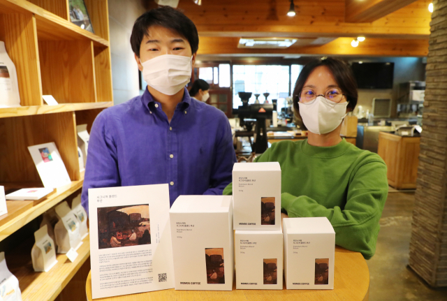 부산 커피 브랜드 ‘모모스’가 부산 토박이 김종식 화백의 작품 ‘귀환동포’를 새겨 넣은 ‘부산 블렌딩’ 패키지를 출시했다. 모모스커피 이현기(왼쪽) 대표와 전주연 이사. 강선배 기자 ksun@