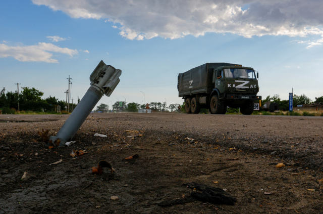 지난달 26일(현지시간) 우크라이나 헤르손 인근 초르노바이우카 한 마을에 떨어진 불발탄 옆을 러시아 군용 트럭이 지나고 있다. 로이터연합뉴스