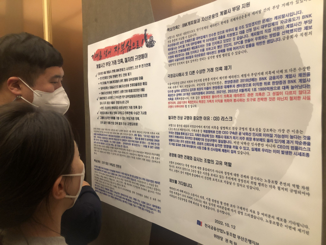 금감원 검사가 시작된 18일 BNK금융 직원들이 부산은행 사내 엘리베이터에 게시된 노조 성명서를 읽고 있다. BNK부산은행 노조 제공