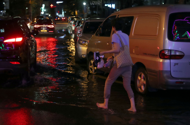 2018년 8월 해수면 상승으로 물이 유입된 경남 창원시 마산합포구 일대 도로에서 한 시민이 신발 등을 손에 들고 걷고 있다. 연합뉴스