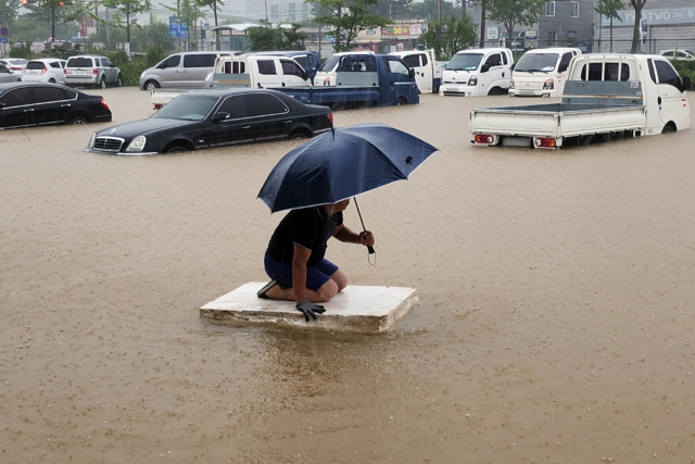 24일 오전 밤사이 내린 폭우에 침수 피해가 난 전남 목포시 석현동 한 중고차 매매단지에서 한 시민이 스티로폼 단열재 조각 위에 올라 물웅덩이를 빠져나가고 있다. 연합뉴스