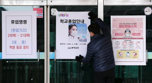 지난 6일 신종코로나 확진자가 거주하거나 이동·체류한 곳과 인접한 서울 성북구의 한 중학교 출입문에서 학교 관계자가 교육청의 휴업 명령과 관련 안내문을 부착하고 있다. 연합뉴스