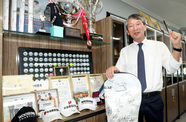 정한식 우성스포츠재단 이사장이 우성종합건설 남자프로골프단 선수들이 고마운 마음을 담아 선물한 ‘사인 캐디백’과 각종 수상 트로피를 배경으로 파이팅을 외치고 있다. 남다른 주택 건설 철학을 가진 그는 “선한 인생이 행복한 인생이라고 생각한다”며 환하게 웃어보였다. 강원태 기자 wkang@