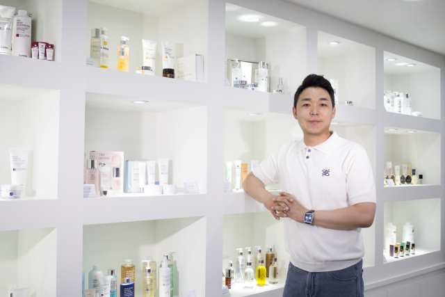 (주)아이피아코스메틱 최재근 대표가 제조 화장품들 앞에서 포즈를 취하고 있다.