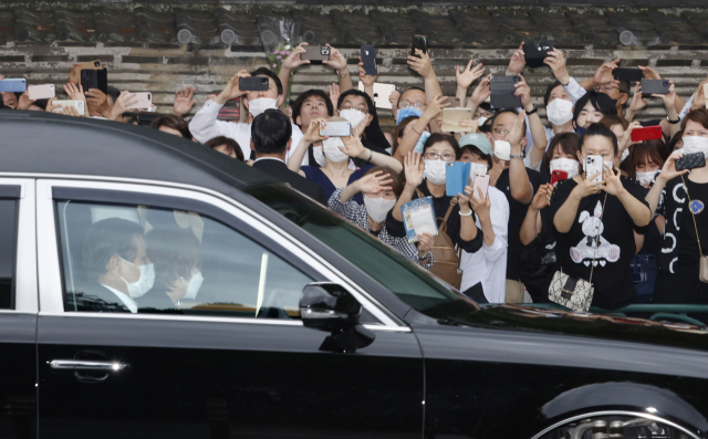 아베 신조 전 총리의 관을 실은 장의차가 12일 오후 일본 도쿄도 미나토구의 사찰 조조지에서 나와 이동할 때 근처에서 시민들이 스마트폰으로 사진을 찍고 있다. 고인이 총리 재임 중 코로나19 확산 방지 대책의 일환으로 배포하도록 지시한 천 마스크인 일명 '아베노마스크'를 든 시민의 모습도 보인다. 아베 전 총리는 이달 8일 나라현 나라시에서 참의원 선거를 앞두고 유세를 하던 중 총을 맞고 목숨을 잃었다. 연합뉴스