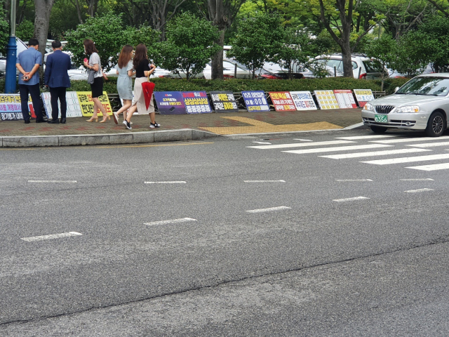 19일 부산 연제구 부산시청 앞에서 공시생 유족이 설치한 패널을 지나가는 시민들이 살펴보고 있다. 유족은 지난해 1년째 부산시교육청과 부산시청 등지에서 패널을 설치하고 1인 시위를 이어가고 있다. 유가족 제공