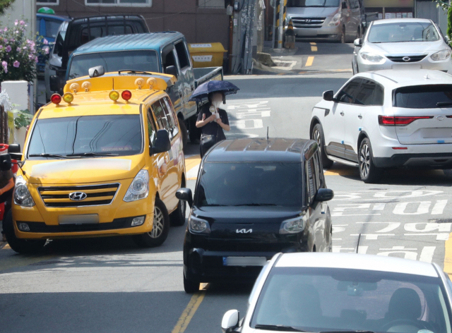 지난 13일 3살 난 어린이가 통학버스에 몸이 끼여 크게 다친 부산 부산진구 사고 현장 인근 좁고 경사진 도로에서 20일 오전 차량과 행인들이 뒤엉켜 지나고 있다. 정대현 기자 jhyun@