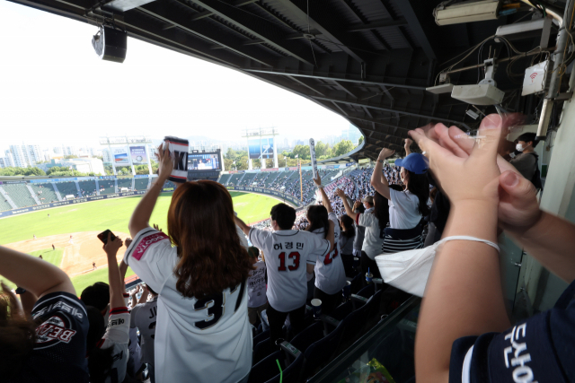 25일 오후 서울 잠실야구장에서 마스크를 팔에 건 한 관중이 프로야구 경기를 관람하고 있다. 26일부터 실외마스크 착용 의무가 완전히 해제된다. 이에 따라 당장 이번 가을 프로야구(포스트시즌)를 비롯해 야외 공연, 대규모 집회 등에서 마스크를 쓰지 않아도 된다. 연합뉴스