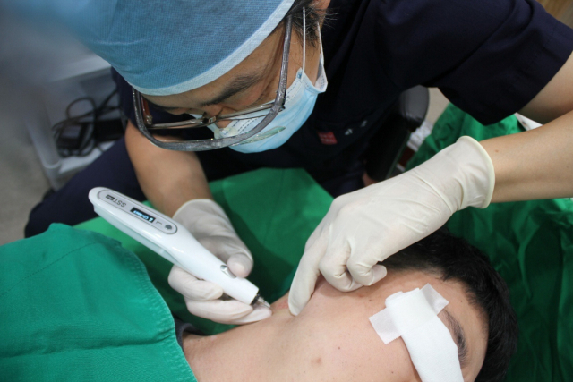 박근 부산해운대센텀모빅스피부과 원장이 전동펀치로 귀 뒤쪽 정상피부를 채취해 백반증에 발병한 곳에 이식하는 ‘미세천공 피부이식술’을 하고 있다. 부산 해운대 센텀모빅스피부과의원 제공