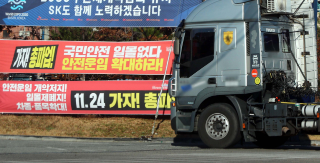화물연대 파업을 하루 앞둔 23일 오후 부산 남구 부산항 신선대부두 인근에 화물연대가 안전운임제 일몰제 폐지 등을 요구하며 내건 현수막 앞으로 화물 차량들이 지나가고 있다. 정종회 기자 jjh@