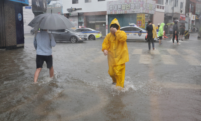 부산에 호우경보가 내려진 지난 11일 오후 부산 수영구 우리은행 망미지점 앞 도로가 폭우에 침수돼 시민들이 물 위를 힘겹게 걸어가고 있다. 정종회 기자 jjh@