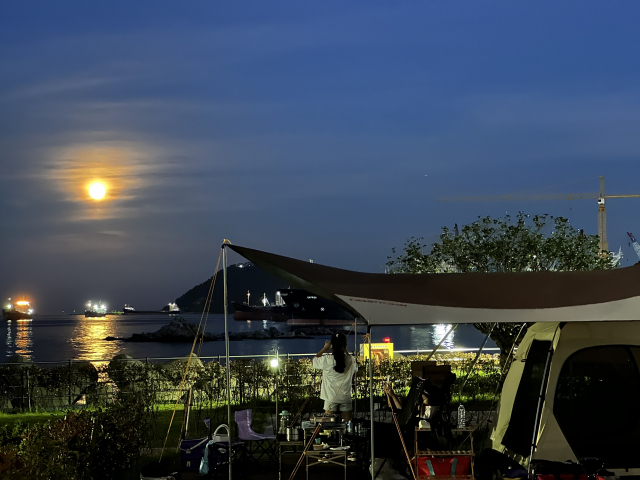 영도마리노오토캠핑장에서 바라본 부산항 앞바다. 밤하늘에 슈퍼 문이 떠올라 자연과 도시의 매력을 두루 보여 준다.