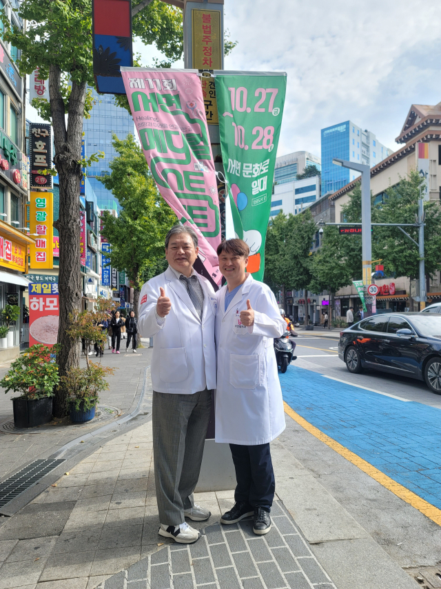 성재영(왼쪽) 이사장과 홍훈표 회장이 제11회 서면메디컬스트리트 축제를 알리는 가로등 배너 앞에서 포즈를 취하고 있다. SMS의료관광협의회 제공