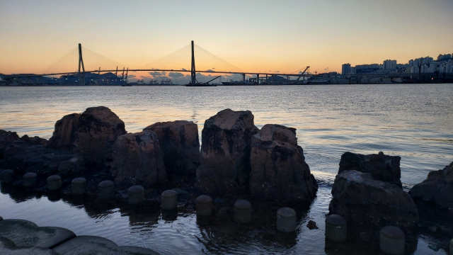 부산 북항 친수공원 수변 산책로에서 바라본 부산항대교. 대교 뒤쪽으로 해가 떠오르기 직전의 붉은 기운이 번지고 있다. 일출 사진을 찍을 때 수변에 자리잡은 갯바위를 포함하면 이색적인 사진이 된다. 김희돈 기자