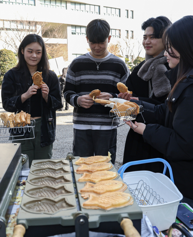 26일 부산 사상구 동서대학교 민석스포츠센터에서 열린 제33회 입학식에 신입생들 입학 축하 붕어빵 나눔 행사가 열려 새내기 대학생들이 활짝 웃으며 붕어빵을 받고 있다. 김종진 기자 kjj1761@