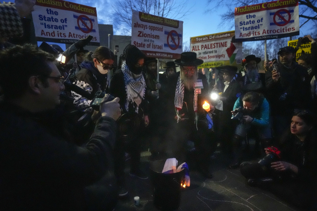 26일(현지시간) 미국 워싱턴D.C. 이스라엘 대사관 앞에서 랍비 복장의 시민 등이 이스라엘 국기에 불을 붙이며 시위하고 있다. 이날 이곳에서는 현역 미 공군 병사가 “학살의 공범이 될 수 없다”고 외치며 자신의 몸에 불을 붙여 자살했다. AP연합뉴스
