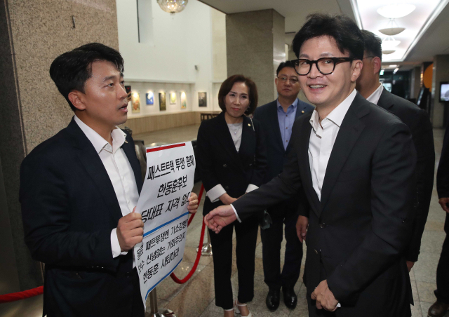 국민의힘 한동훈 당 대표 후보가 18일 서울시의회에서 열린 국민의힘 서울시의회 의원간담회에 참석하기에 앞서 ‘패스트트랙 투쟁 폄훼 한동훈 후보 당대표 자격 없다’가 적힌 피켓을 든 이희원 서울시의원과 대화하고 있다. 연합뉴스