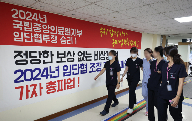 26일 오전 서울 중구 서울국립중앙의료원에서 의료진이 전국민주노동조합총연맹 전국보건의료산업노동조합 국립중앙의료원지부가 붙인 총파업 관련 현수막을 지나치고 있다. 연합뉴스