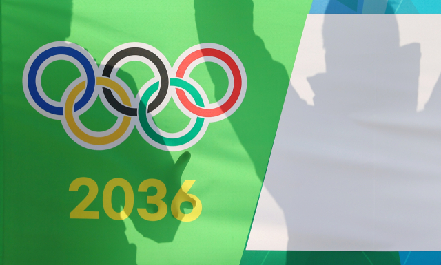 대한체육회 대의원총회를 통해 2036 하계 올림픽에 도전할 국내 유치 도시가 결정되는 28일 총회를 앞둔 서울 송파구 올림픽파크텔 앞에서 응원전을 펼치는 한 관계자의 모습이 오륜마크와 2036 숫자 위로 비치고 있다. 연합뉴스