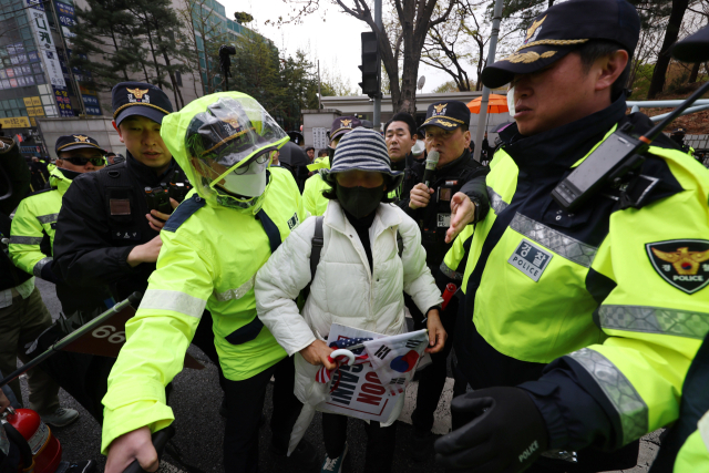 내란 우두머리 혐의로 기소된 윤석열 전 대통령의 첫 형사재판이 열린 14일 서울 서초구 서울중앙지방법원 앞에서 경찰 관계자들이 한 윤 전 대통령 지지자를 윤 전 대통령 엄벌 촉구 기자회견을 하는 시민단체와 분리하고 있다. 연합뉴스