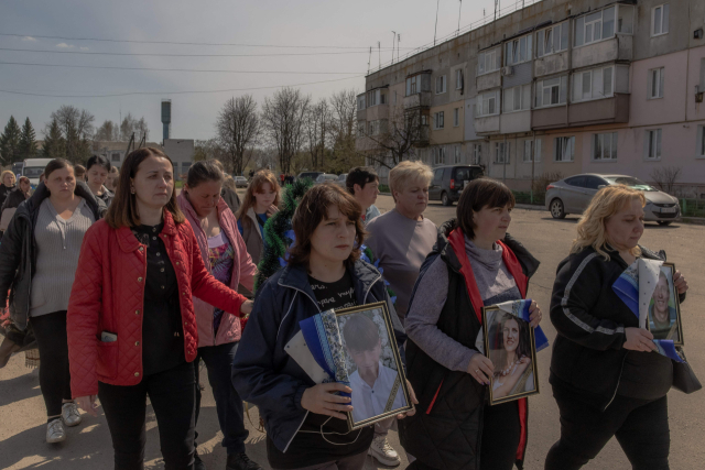 16일(현지 시간) 우크라이나 북동부 수미 외곽에서 열린 장례식에서 참석자들이 지난 13일 러시아의 미사일 공격으로 숨진 11살 아이와 부모의 사진을 들고 마을을 지나가고 있다. 이 공격으로 최소 35명이 숨졌다. AFP연합뉴스