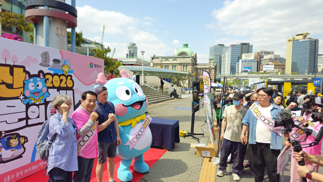 나동연 양산시장이 21일 서울역 광장에 설치한 2026년 양산 방문의 해 홍보관에서 시 관광 캐릭터인 ‘뿌용’과 미국에서 온 외국인 부부와 함께 ‘화이팅’을 외치며 기념사진을 찍고 있다, 앞쪽에는 시민들이 뿌용 등과 사진을 찍기 위해 대기하고 있다. 김태권 기자