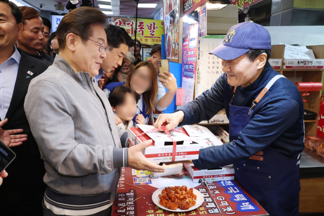 더불어민주당 이재명 대선 후보가 '골목골목 경청투어' 사흘째인 3일 '동해안벨트' 첫 방문지인 강원도 속초시 중앙재래시장에서 닭강정을 구입하며 상인과 대화하고 있다. 연합뉴스