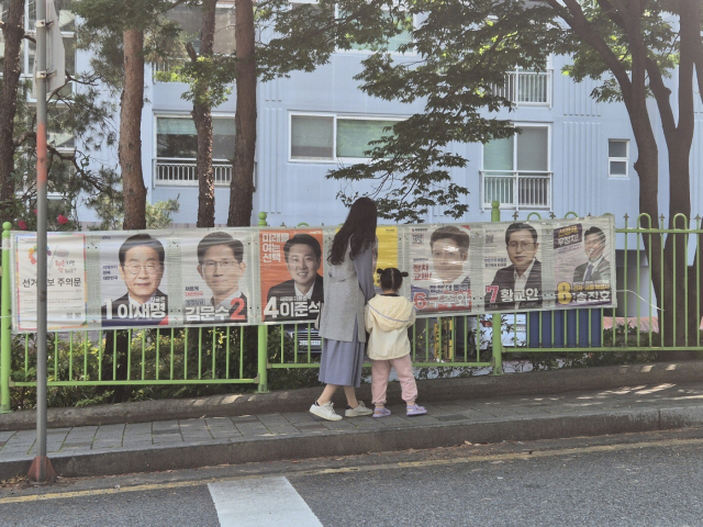 25일 울산시 남구 신정동 한 아파트 단지 앞 인도에서 한 모녀가 손을 잡고 걷다가 선거벽보를 보며 이야기를 나누고 있다.