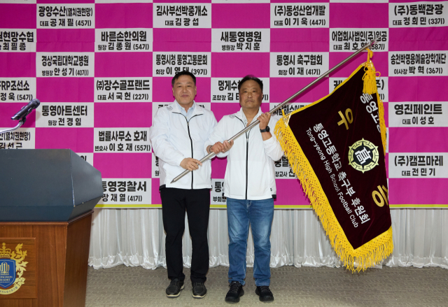 통영고등학교 축구부 공재필(오른쪽) 신임 후원회장이 지난달 17일 열린 회장 이·취임식에서 문현호 직전 회장으로부터 후원회 기를 전달받고 있다.