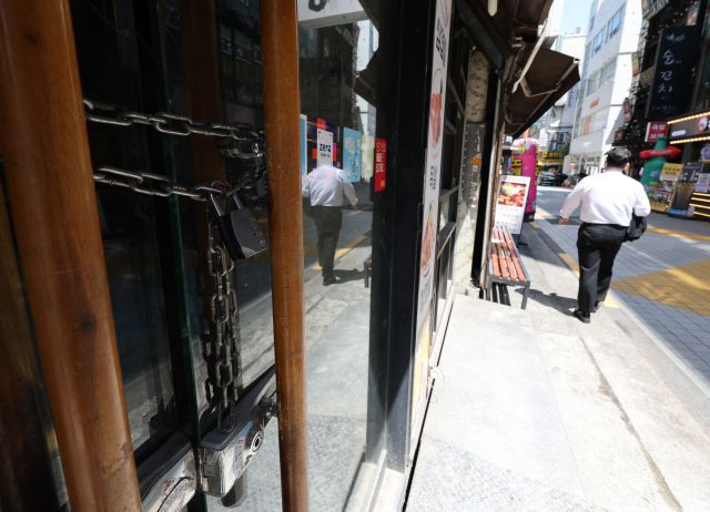 심각한 내수 침체로 은행에서 빌린 돈을 갚지 못하는 한계 기업과 가계가 빠르게 늘어나고 있다. 영업을 중단하고 문을 걸어 잠근 상점 옆으로 사람이 걸어가고 있다. 연합뉴스