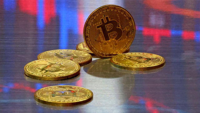 비트코인 모형이 놓인 바닥에 코인 시세 그래프가 비치는 모습. 연합뉴스 제공