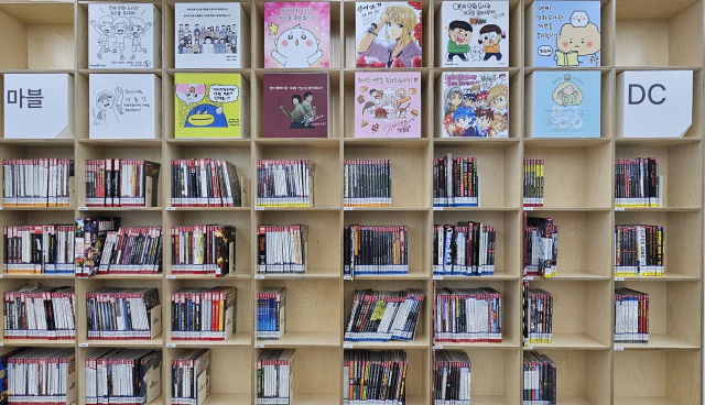 만화 라운지 책장에 꽂힌 마블·DC 코믹스 만화책들. 상단에 있는 유명 웹툰 작가들의 축전도 눈길이 간다.