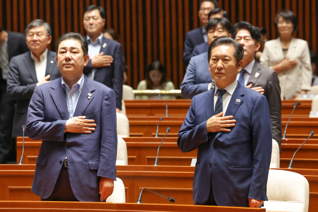 더불어민주당 정청래 대표(오른쪽)와 김병기 원내대표가 21일 국회에서 쟁점법안 처리를 위한 8월 임시국회 본회의 개회를 앞두고 가진 의원총회에서 국기에 경례하고 있다. 연합뉴스
