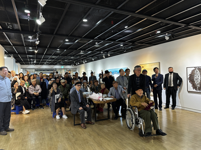 21일 금련산역갤러리에서 열린 ‘서재만 회고전: 묻혔습니다' 개막식 후 참석자들이 기념사진을 찍고 있다. 맨 앞 휠체어를 타고 있는 이가 서재만 화백이다. 김은영 기자 key66@
