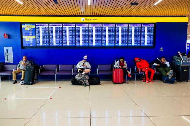 미국 연방정부 셧다운 사태 장기화로 연방항공청(FAA)이 항공편 운항 감축을 지시하면서 항공편들이 줄줄이 지연되거나 취소되는 가운데 8일(현지 시간) 이를 알리는 콜로라도주 덴버 국제공항 현광판 앞에 사람들이 앉아있다. AFP연합뉴스