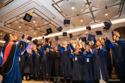 수료생들이 축하를 나누며 모자를 던지고 있다.