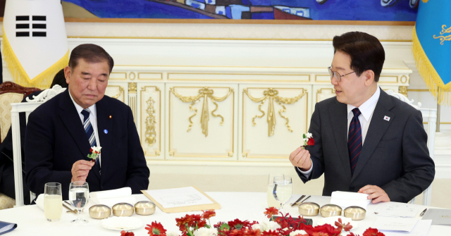 이재명 대통령과 이시바 시게루 전 일본 총리가 8일 청와대에서 오찬 전 자리에 놓인 꽃을 들고 대화하고 있다. 연합뉴스