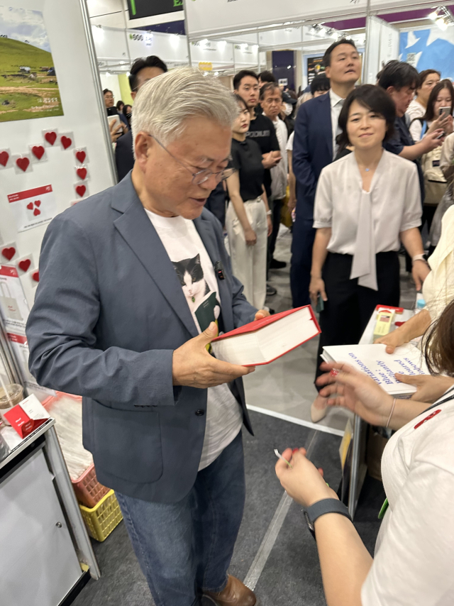최근 막을 내린 '2026 서울국제도서전'에서 부산출판문화산업협회 연합 부스를 찾은 문재인 전 대통령이 정철교 작가의 새 책 <붉은 선으로 가둔 하루들, 나의 2021년>을 뮤트스튜디오 이보리 대표로부터 건네받고 있다. 공교롭게도 정 작가가 울산 울주군 서생면으로 옮겨가기 전 살았던 경남 양산시 매곡동 작업실은 문 전 대통령 옛 사저로 사용되는 인연이 있었다. 뮤트스튜디오 제공
