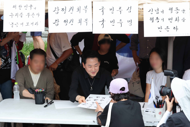 6·3지방선거 투표용지 부족 사태로 촉발된 잠실 개표소 봉쇄 시위가 이어진 17일 국민의힘 장동혁 대표가 서울 송파구 올림픽공원 핸드볼경기장 앞에서 집회 참가자들에게 붓글씨를 써주고 있다. 연합뉴스