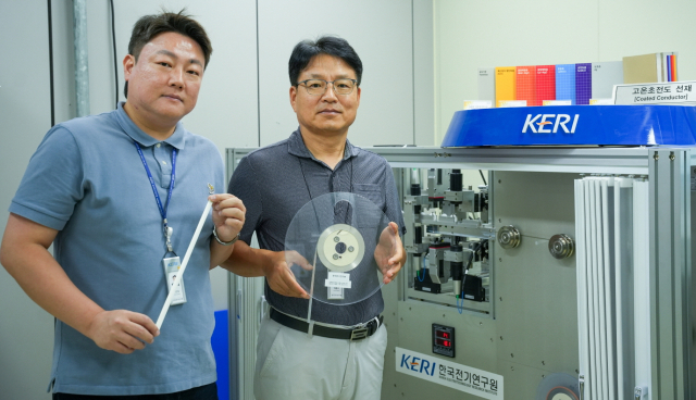 전기연구원(KER)I 박인성(왼쪽)·하홍수 박사가 고온초전도 선재를 들고 3D 비접촉 초정밀 검사 장비 옆에서 포즈를 취하고 있다. KERI 제공